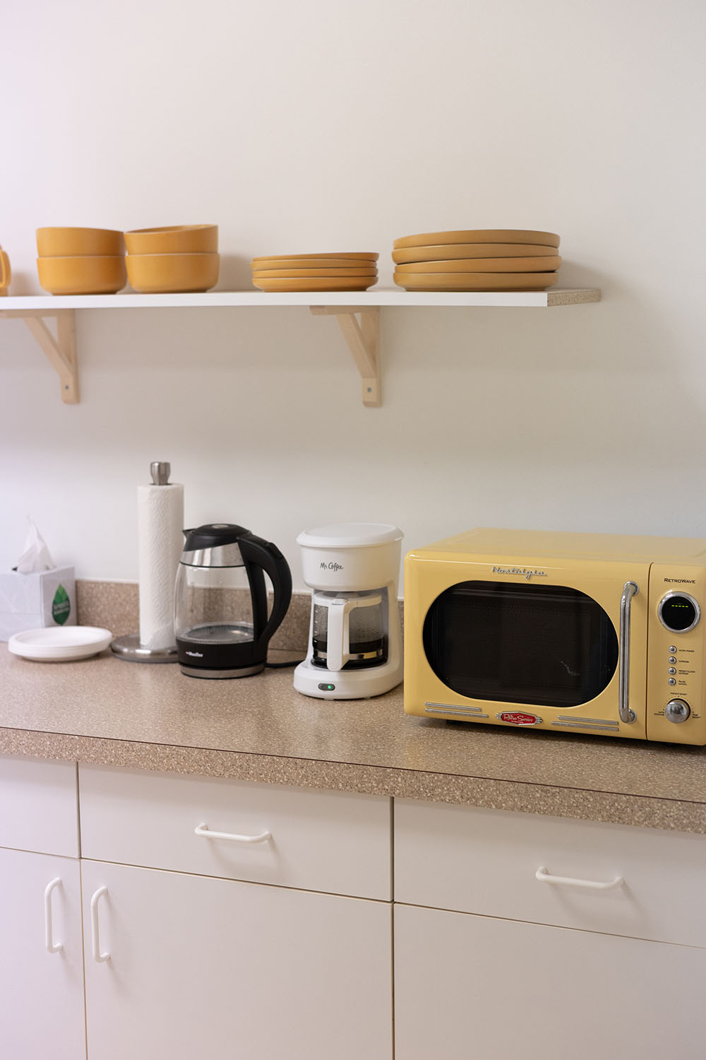 Yellow microwave on a kitchen counter with shelves above containing bowls.